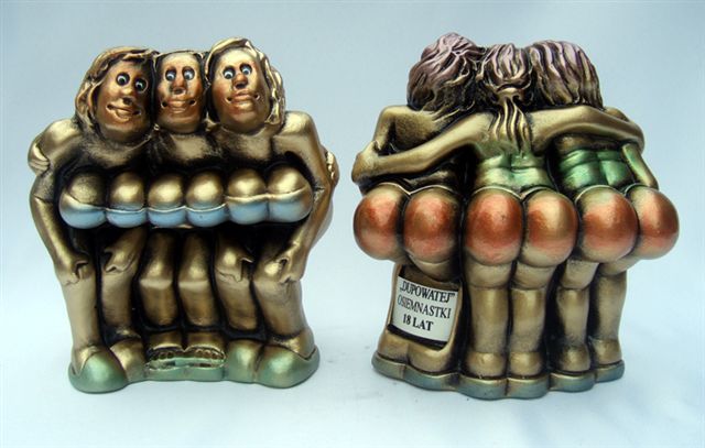 Dwie rzeźby z brązu przedstawiające trzy nagie kobiety obejmujące się, z przodu widoczne piersi a z tyłu pośladki; na jednej rzeźbie widoczna kartka z napisem 'Dupowatej osiemnastki 18 lat'.